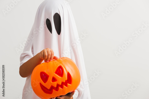 Funny Halloween Kid Concept, little cute child with white dressed costume halloween ghost scary he holding orange pumpkin ghost on hand, studio shot isolated on white background © sorapop