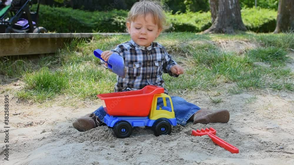 Happy little child having fun playing with sand and colorful toys in the park, beautiful summer sunny day in children playground Happy little child having fun playing with sand and colorful toys in the park, beautiful summer sunny day in children playground