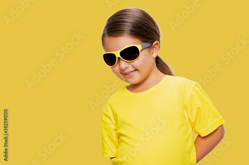 Happy child. Cheerful Little Girl wearing sunglasses Happy Smiling Studio Concept. yellow background. isolated  © Julia