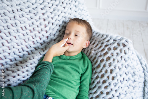 Bol'nyy mal'chik s termometrom lezhal v posteli i mat' ruki prinimaya temperaturu. Mama proveryayet temperaturu svoyego bol'nogo syna, u kotorogo vo rtu termometr. Bol'nyy rebenok s likhoradkoy i bol photo
