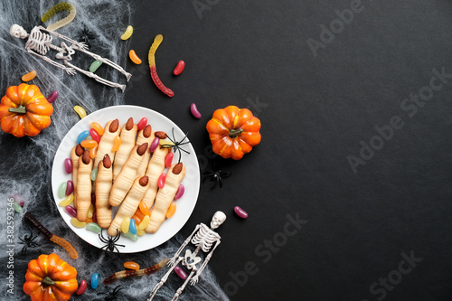 Happy Halloween holiday concept. Halloween cookies in form of witches fingers, pumpkins, skeletons, spiderweb, festive decorations on black background. Flat lay, top view.