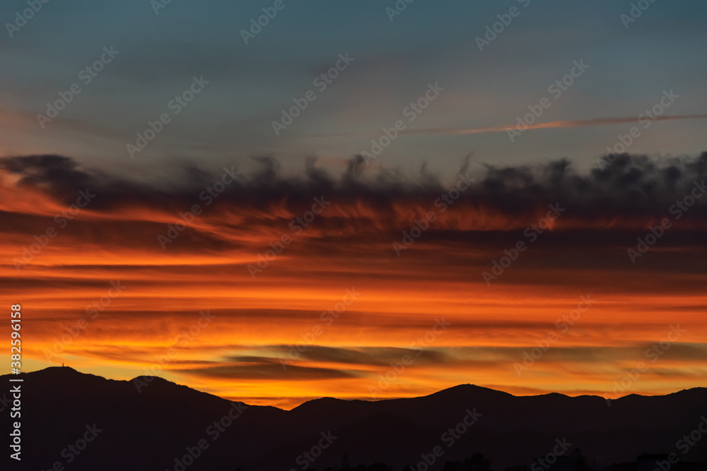 a close up of fire coloured clouds during sunset with a  mountain range silhouette  below
