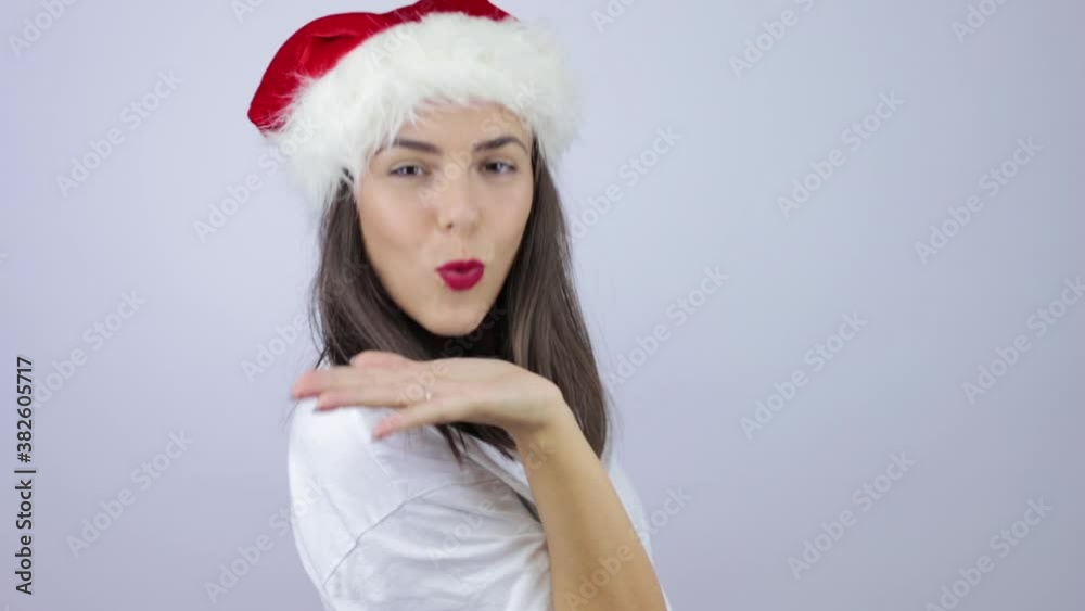 Young beautiful woman wearing Santa Claus hat over isolated white background appearing by surprise, sending a kiss to the camera and leaving again Young beautiful woman wearing Santa Claus hat over isolated white background appearing by surprise, sending a kiss to the camera and leaving again