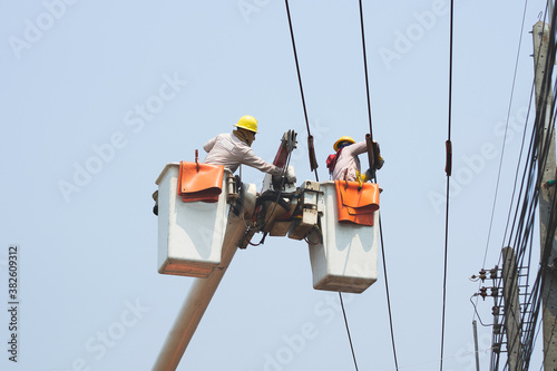 Electricians work together on the electric cable car and electric pole. To maintain the high and low voltage distribution system. They wear a helmet with PPE protection and copy space for your text.