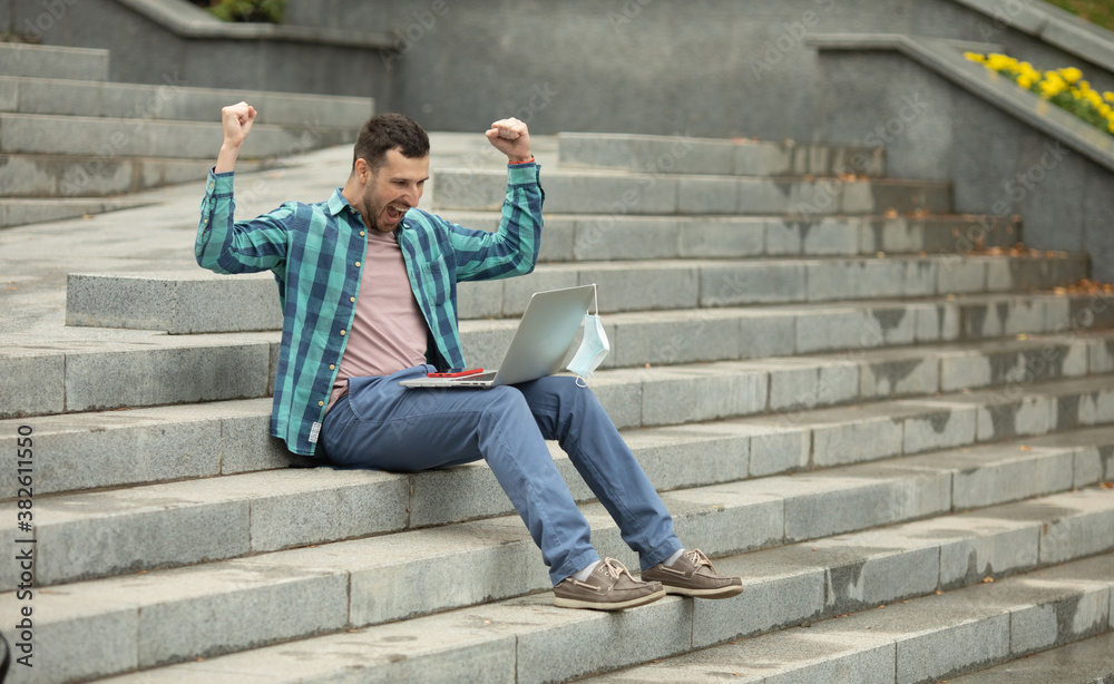 Portrait of a happy young man using laptop and celebrating sitting outdoor on stairs. Portrait of a happy young man using laptop and celebrating sitting outdoor on stairs.