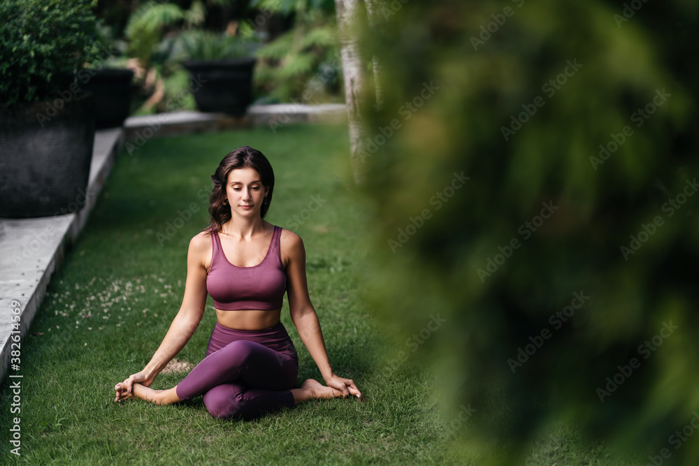 Woman practicing yoga performing yoga-asanas outdoors. Young attractive slim fitness girl in bodysuit relaxing and doing exercises. Woman practicing yoga performing yoga-asanas outdoors. Young attractive slim fitness girl in bodysuit relaxing and doing exercises.