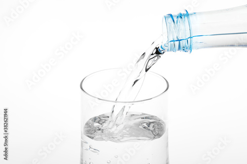 Pouring water from plastic bottle into glass on white background.
