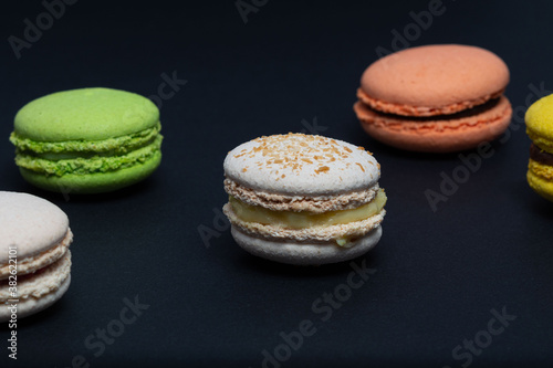 Delicious red, green, white and yellow macaroni are arranged diagonally in two rows against a black background. Side view