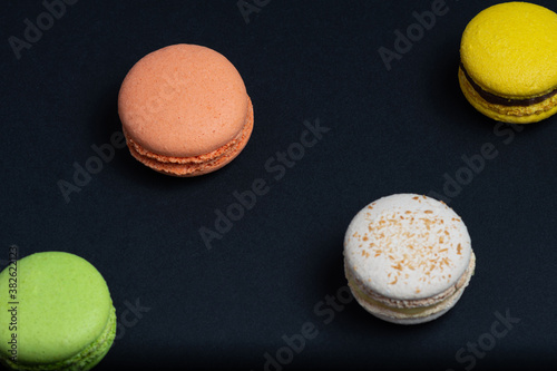 Delicious red, green, white and yellow macaroni are arranged diagonally in two rows against a black background. View from above