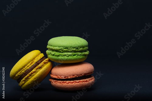 Macaroni, red, yellow, green, are stacked one on top of the other in the form of a tower on a black background. Side view