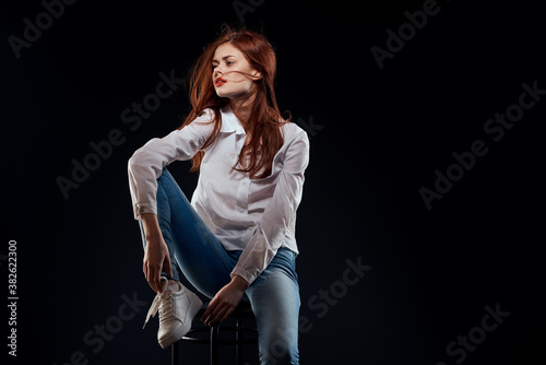 pretty woman sitting on a chair posing white shirt jeans long hair red lips dark background