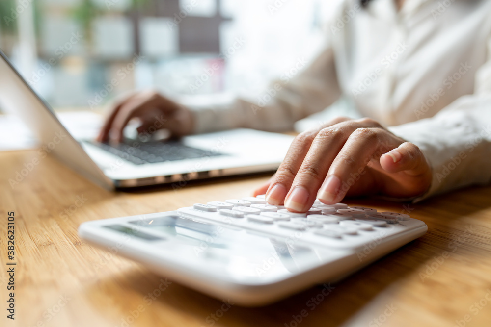 Asian business accounting female hand working on desk office with using a calculator pen and laptop accountant or banker making calculations.HOME Savings economy expenses finance accounting concept.
