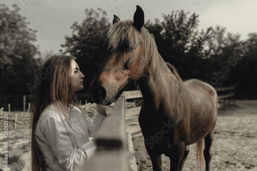 beautiful girl in a white shirt stroking her white horse over the fence at the ranch. cinematic photography