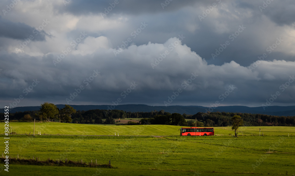 roter Bus auf Landstraße unter dramatischem Himmel