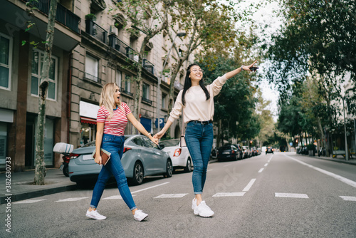 Happy female best friends enjoying together vacations for exploring city during international trip, cheerful female travellers choosing destination route while walking at touristic street and smiling