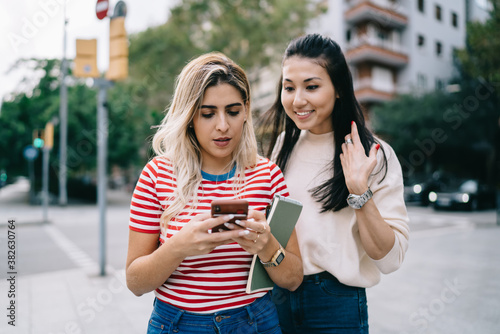 Multiracial hipster girls enjoying mobility chatting and messaging during city sightseeing on vacations, charming female bloggers using smartphone for making online booking and travel ticketing