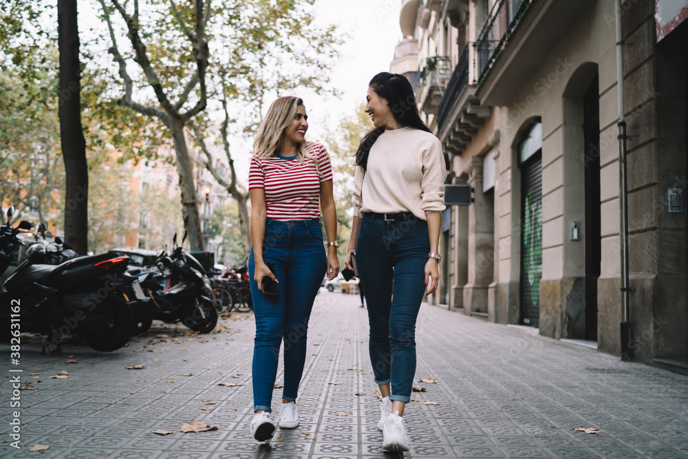 Funny female best friends enjoying together vacations for exploring new city during international trip, charming female tourists discussing destination route while walking at urban street and smiling