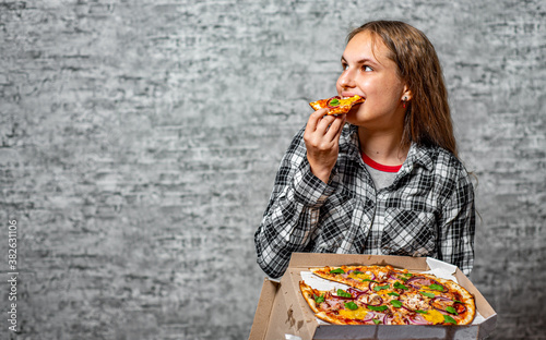 portrait of young teenager brunette girl with long hair hold pizza in box on gray wall background