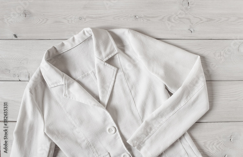 White women's short linen jacket with buttons and long sleeves. Women's elegant clothing on a light wooden background. For mockup.