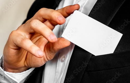 Part of body of man who takes out business card from the pocket of business suit, copyspace. Businessman in black business suit puts white card in pocket. Business concept.