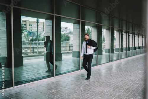 Cheerful worker walking along modern building © BullRun