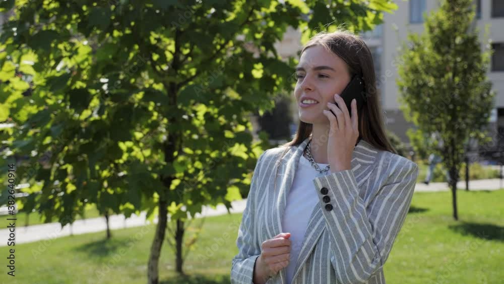 Attractive girl in a light jacket stands outdoors and speaks on the phone. She smiles sincerely. Global network, internet, application. Attractive girl in a light jacket stands outdoors and speaks on the phone. She smiles sincerely. Global network, internet, application.