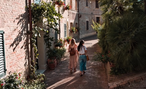 A couple of girls is walking in an italian medieval village with plants and flowers on the street (Corinaldo, Marche, Italy, Europe) © Tommaso