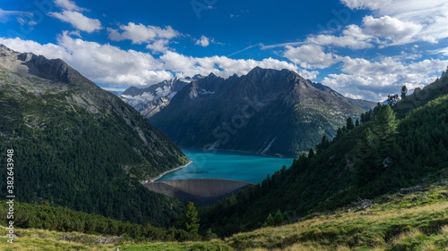 Emerald blue water dam in Alpine mountain range with blue sky and forest