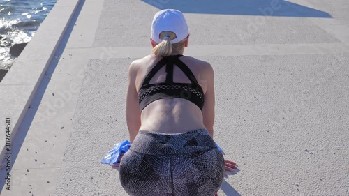 A young woman in sportswear rests between workouts on the seafront early in the morning.

