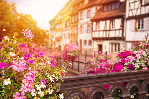 Defocused background with scenic french old town architecture. View on blurred Colmar village with flowers by foreground  sunshine. Romantic place for travel destination. Alsace  France