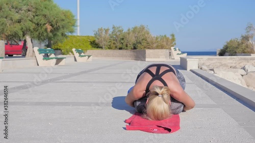 A young woman in sportswear doing back exercise training on the seafront early in the morning.
