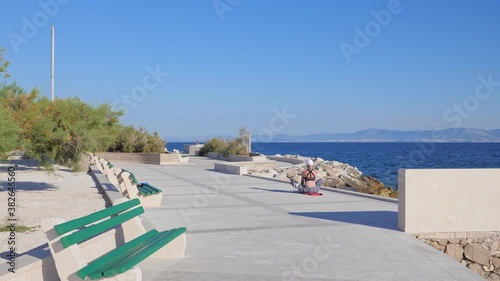 A young woman in sportswear doing cobblers stretch exercise training on the seafront early in the morning.
