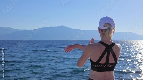 A young woman in sportswear doing shoulder cross stretch and overhead triceps stretch exercise training on the seafront early in the morning.

