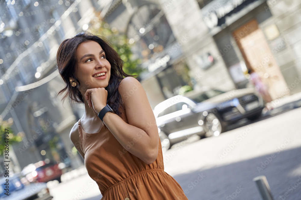 Portrait of a young attractive happy woman wearing summer dress looking aside and smiling while walking on the city streets on a sunny day