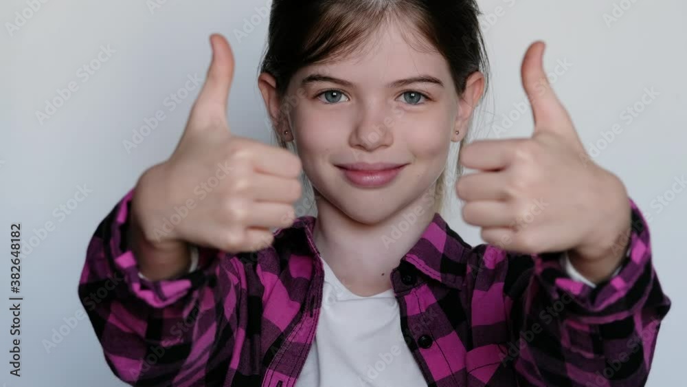 little / young cheerful smiling girl in a pink plaid shirt showing thumb up, ok sign. On white background. little / young cheerful smiling girl in a pink plaid shirt showing thumb up, ok sign. On white background.