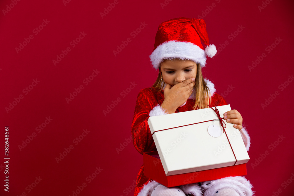 Portrait of a thinking young girl with a open gift box isolated over red background, dressed in santa hat and costume Portrait of a thinking young girl with a open gift box isolated over red background, dressed in santa hat and costume