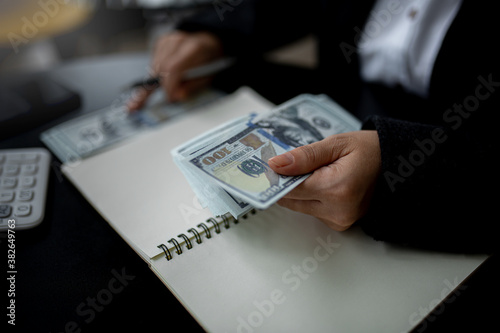 Closeup of business woman hands counting US dollar cash on the table.people holding Us dollar banknotes money ,using calculator calculate saving money with happy in office.