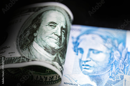 detail of a banknote of 100 reais from brazil beside a hundred dollar bill of american dollars, gloomy scenario, crisis, economic devaluation, punctual focus
