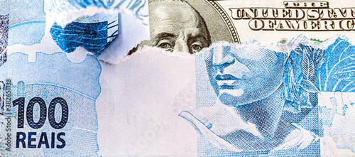 detail of a banknote of 100 reais from brazil beside a hundred dollar bill of american dollars, gloomy scenario, crisis, economic devaluation, punctual focus