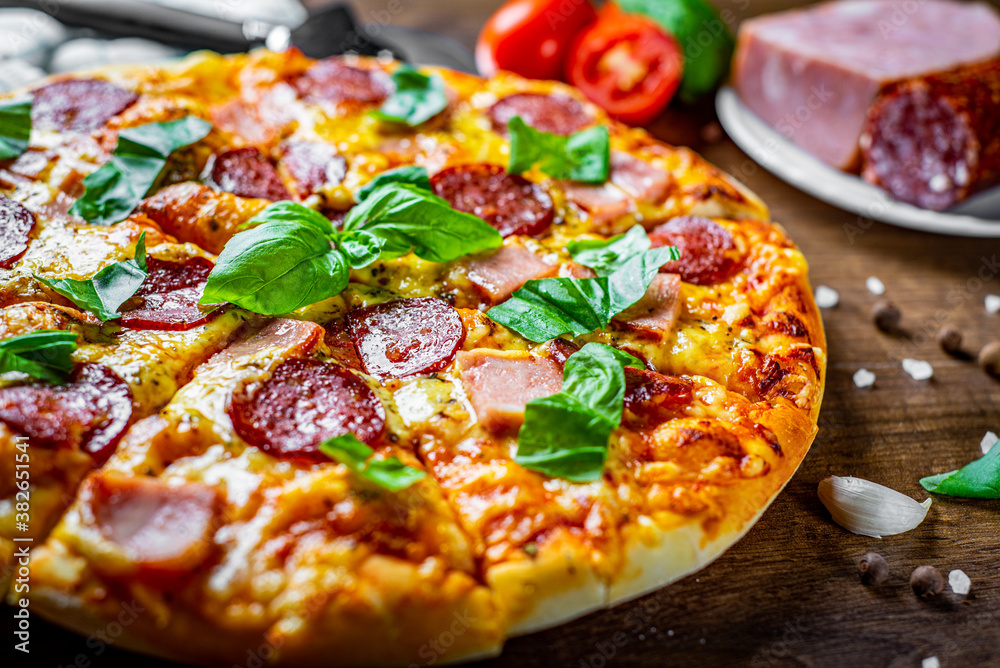Pepperoni Pizza with Mozzarella cheese, salami, ham, Spices and Fresh basil. Italian pizza on wooden table background