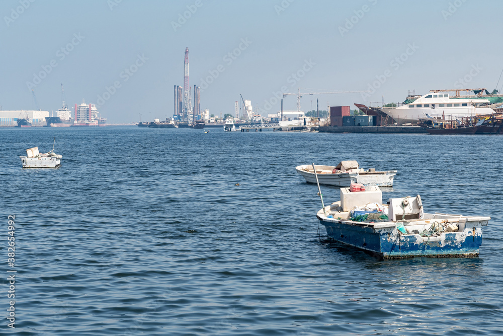 Empty fishing boats on the sea, waiting for its net catch during daytime in the Middle East with industrial structures in the background