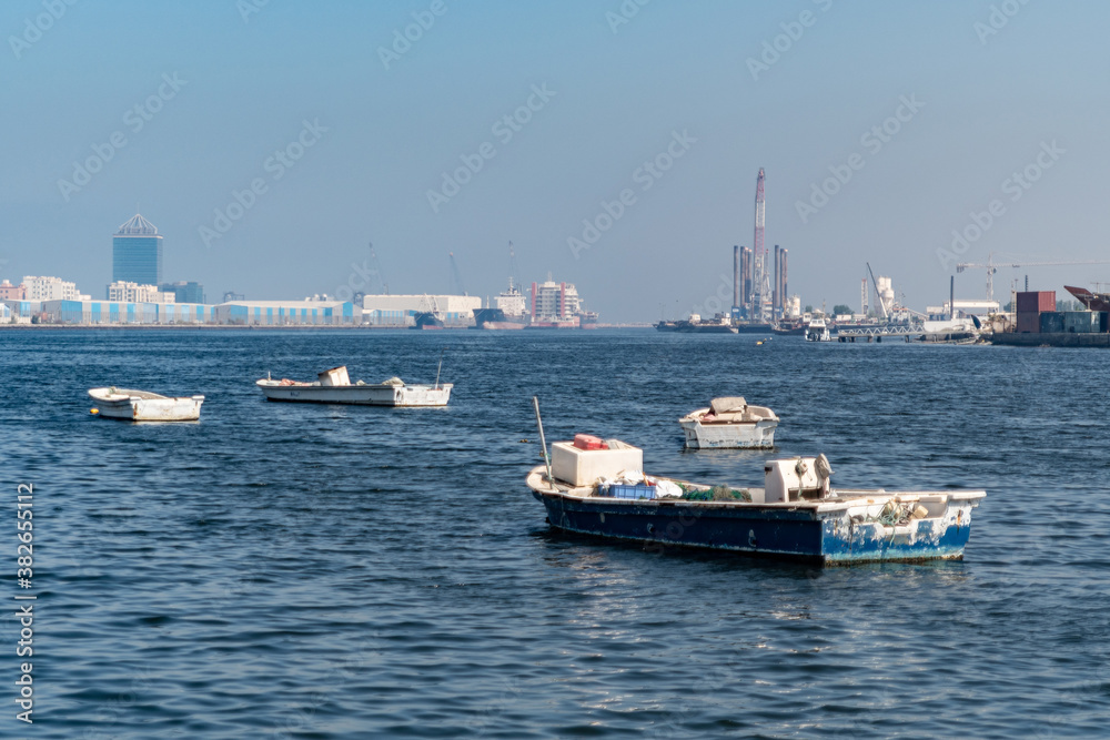 Empty fishing boats on the sea, waiting for its net catch during daytime in the Middle East with industrial structures in the background