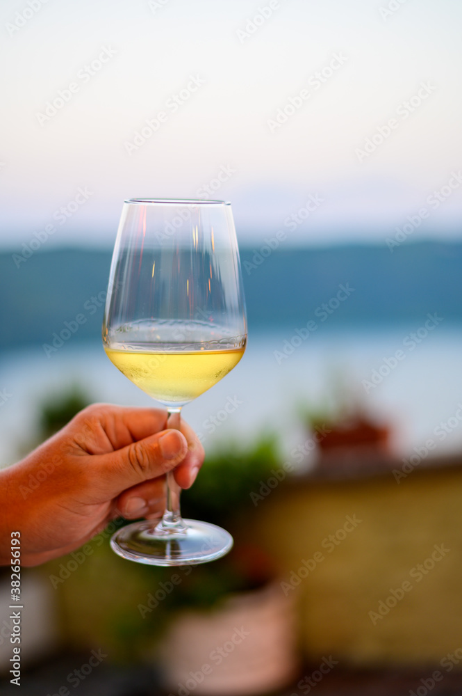 Hand with glass of cold dry white wine served outdoor in cafe at night in Italy