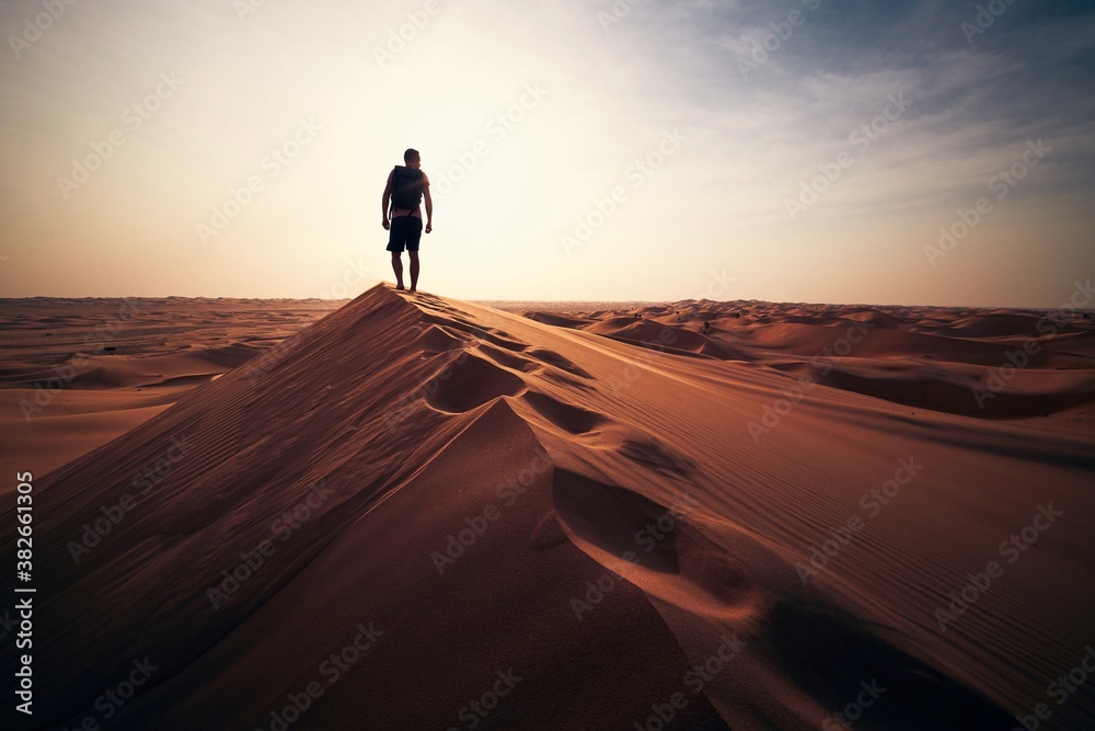 Man walking on sand dune against sunset