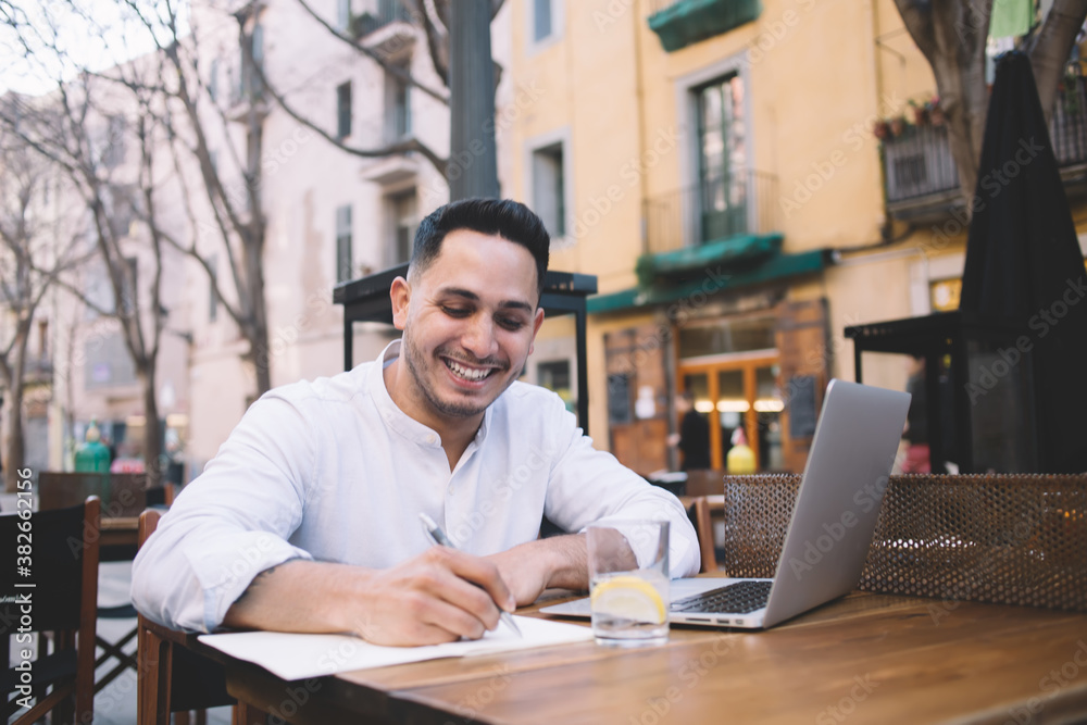 Male freelancer writing in notebook while working from street cafe