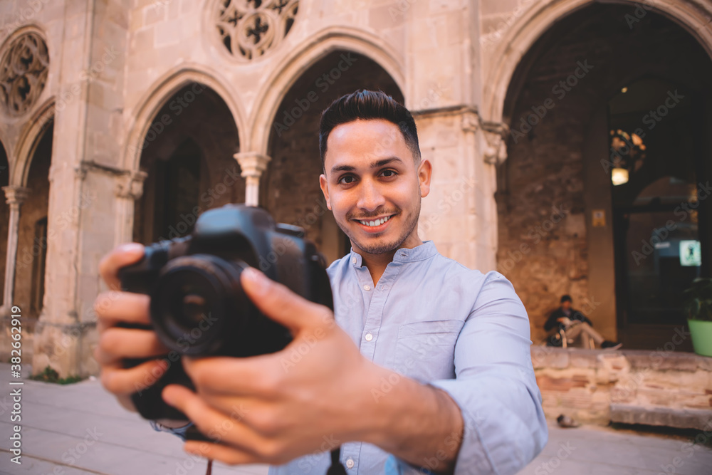 Cheerful ethnic man taking photos of medieval building