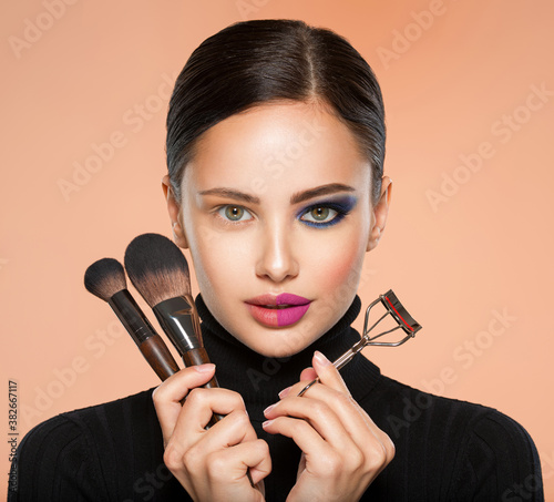 Portrait of a girl with  tools for making makeup near face.  One half face of a beautiful white woman with  bright makeup. Woman holds makeup brush and eyelash curler. 