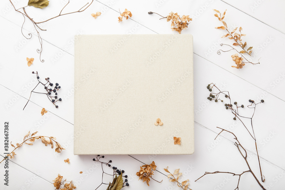 Elegant beige book with linen cover on white wooden background. Wedding photobook. Wedding photo album with autumn dried leaves and plants. School and autumn background. Fall mock up. Thanksgiving day