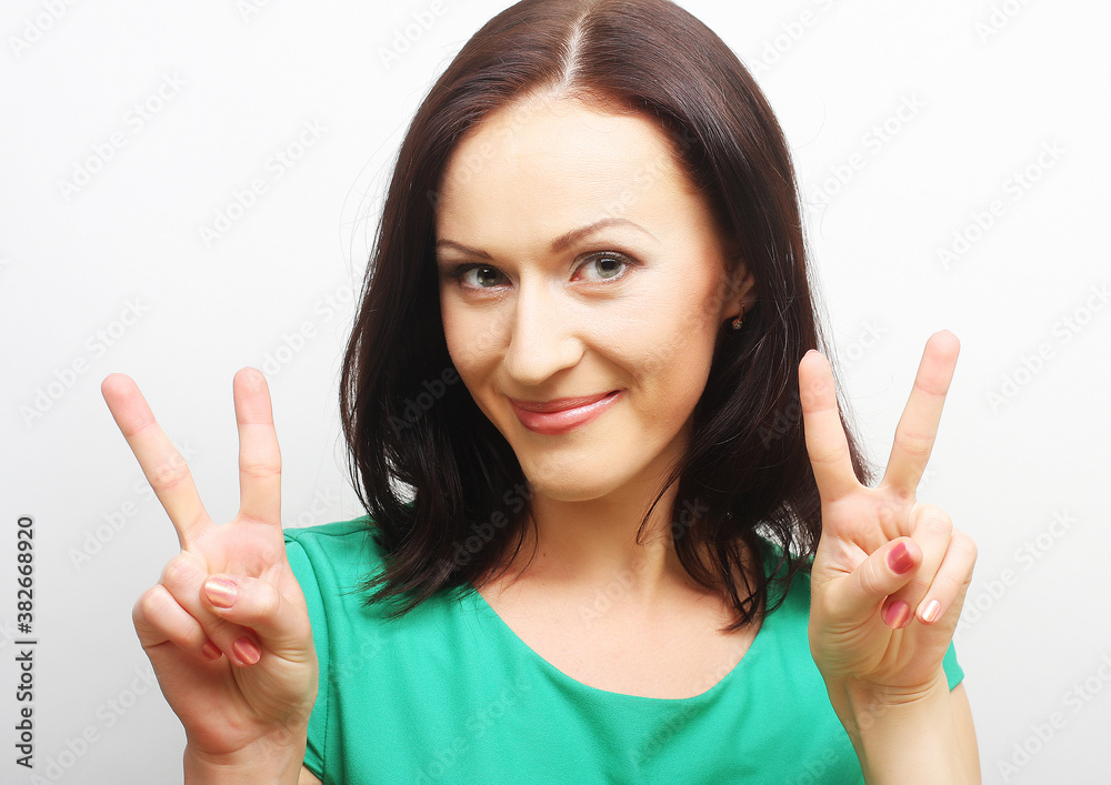 Happy smiling beautiful young woman showing two fingers or victo Happy smiling beautiful young woman showing two fingers or victo