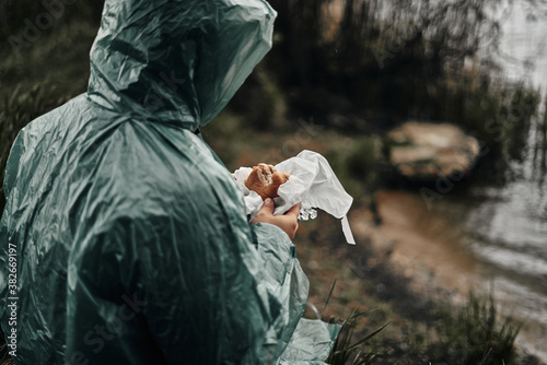 A man with a beard in a green raincoat eats in nature. Cloudy weather, fast food.